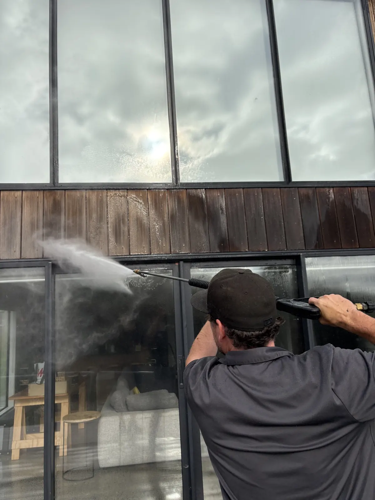 Soft-wash spray rinsing dark stained vertical cedar cladding above sliding doors