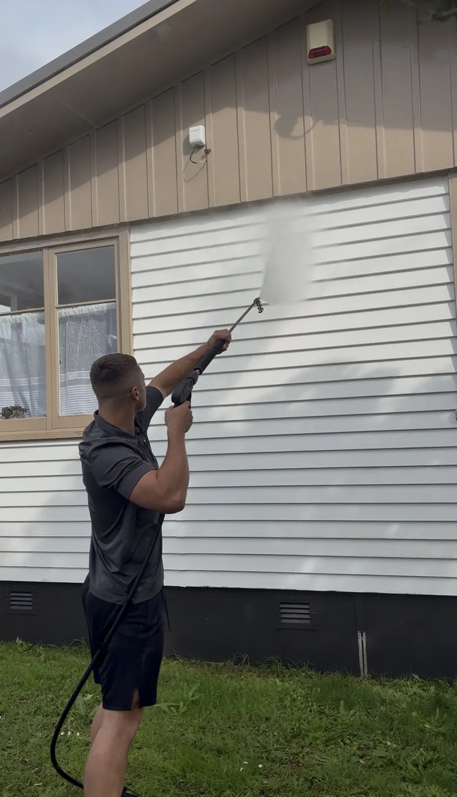 Cleaned band of white weatherboard beside untreated cladding during a house wash