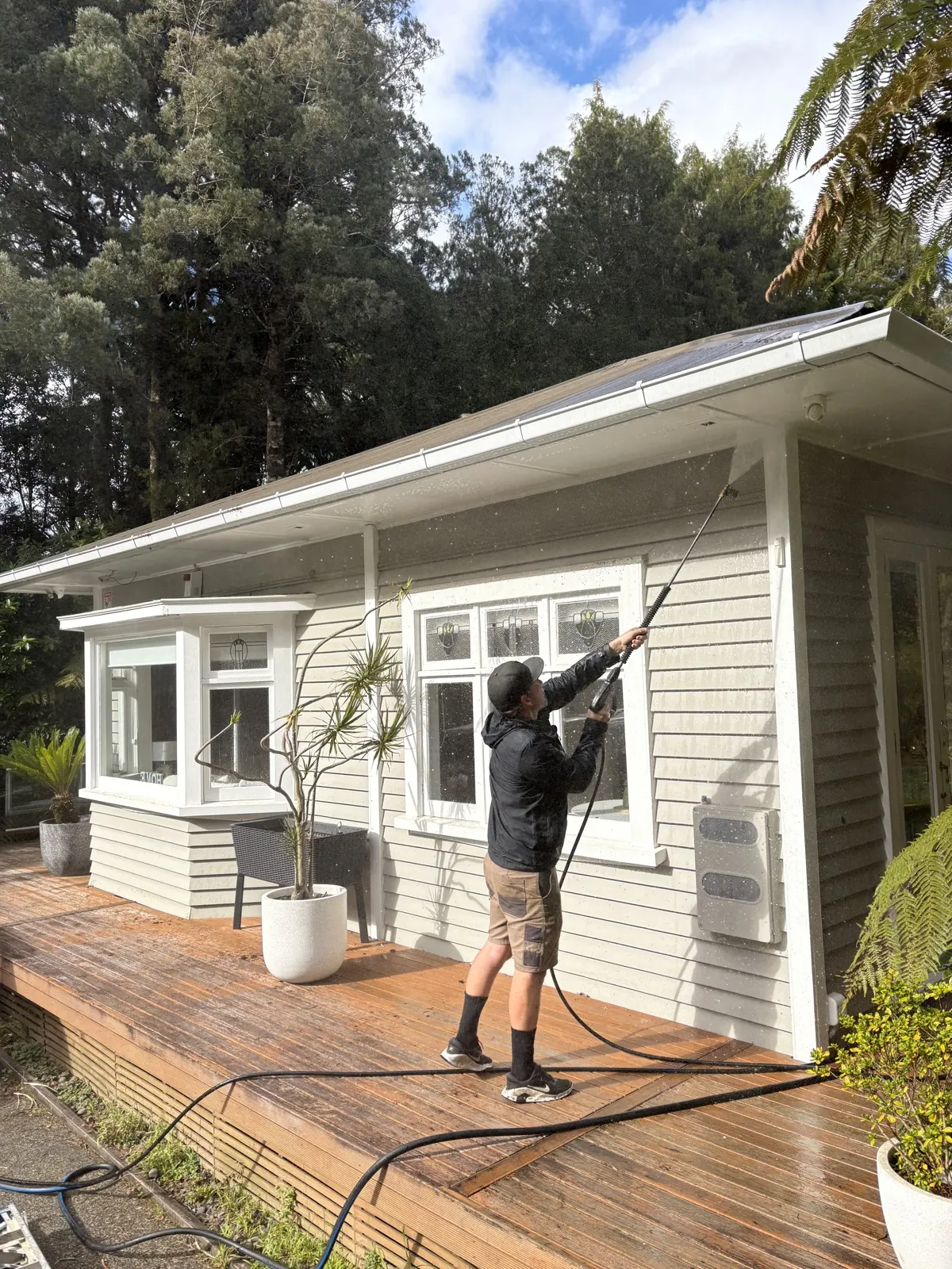 Soft washing the weatherboard cladding of a bush-backed West Auckland home from the deck