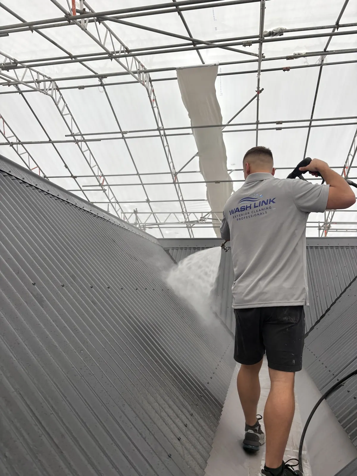 Wash Link technician washing a corrugated metal roof under scaffolding